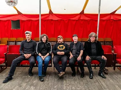 A band seated on red chairs in front of a colorful tent, creating a vibrant and inviting atmosphere.